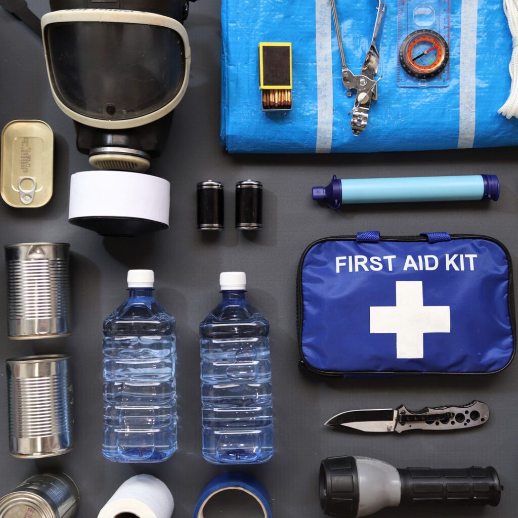 Emergency preparedness kit with bottled water, canned food, flashlight, first aid kit, and survival tools for winter storms.